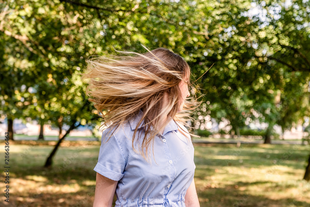 Young caucasian blond woman in a blue stripped summer dress shaking her hair in the park outdoors in a sunny day Young caucasian blond woman in a blue stripped summer dress shaking her hair in the park outdoors in a sunny day