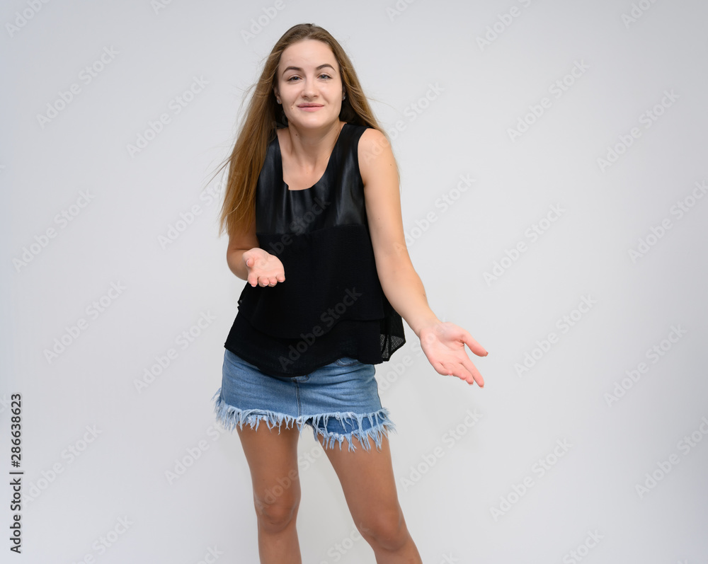 Studio photo portrait of a pretty student girl, young brunette woman with long beautiful hair in denim shorts and a black T-shirt on a white background. Smiling, talking, showing emotions Studio photo portrait of a pretty student girl, young brunette woman with long beautiful hair in denim shorts and a black T-shirt on a white background. Smiling, talking, showing emotions