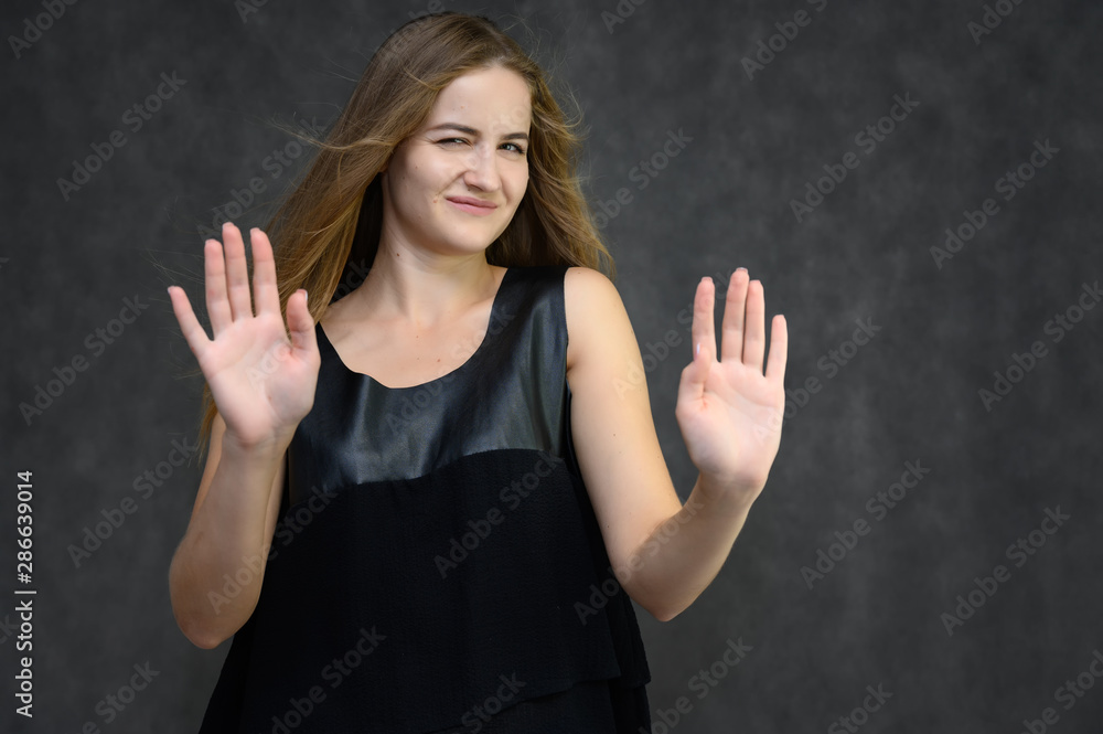Studio photo portrait of a pretty student girl, brunette young woman with long beautiful hair in a black T-shirt on a gray background. Smiling, talking, showing emotions Studio photo portrait of a pretty student girl, brunette young woman with long beautiful hair in a black T-shirt on a gray background. Smiling, talking, showing emotions