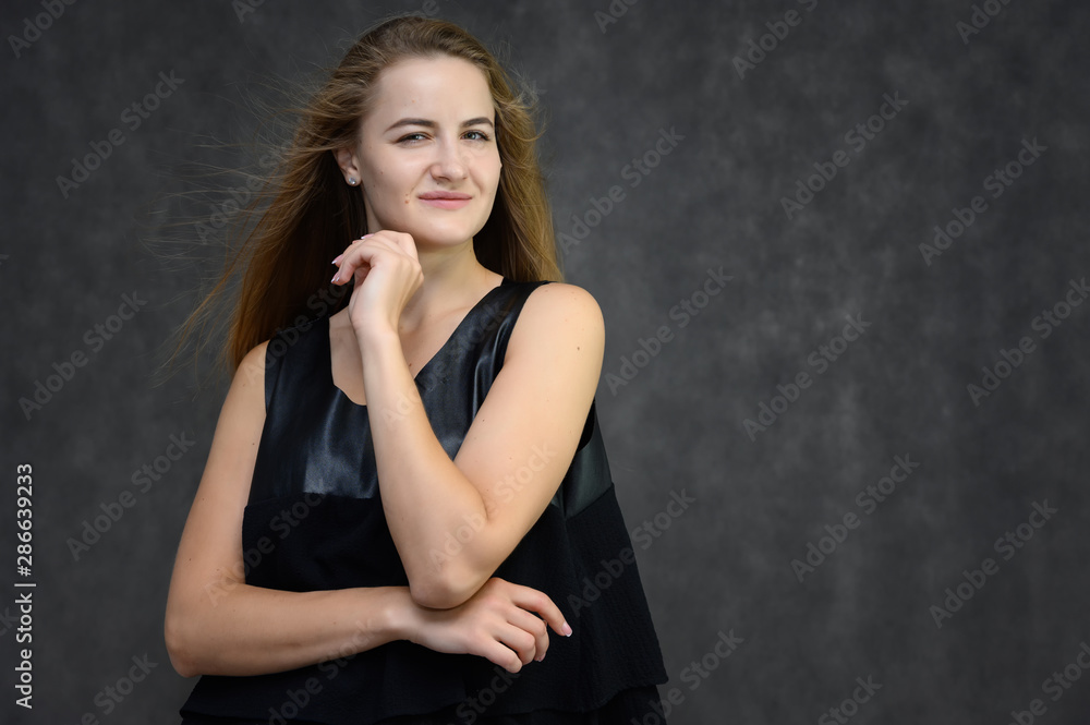 Studio photo portrait of a pretty student girl, brunette young woman with long beautiful hair in a black T-shirt on a gray background. Smiling, talking, showing emotions Studio photo portrait of a pretty student girl, brunette young woman with long beautiful hair in a black T-shirt on a gray background. Smiling, talking, showing emotions