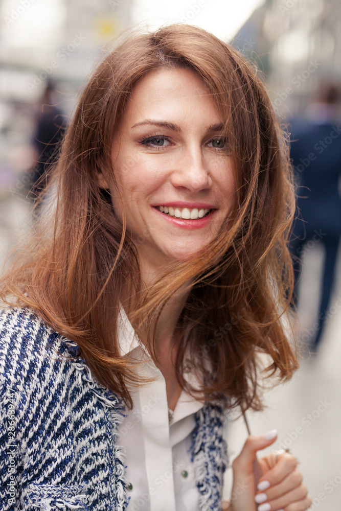 Close portrait of elegant beautiful young smiling brunette woman with messy long hair scattered by the wind standing on the street Close portrait of elegant beautiful young smiling brunette woman with messy long hair scattered by the wind standing on the street