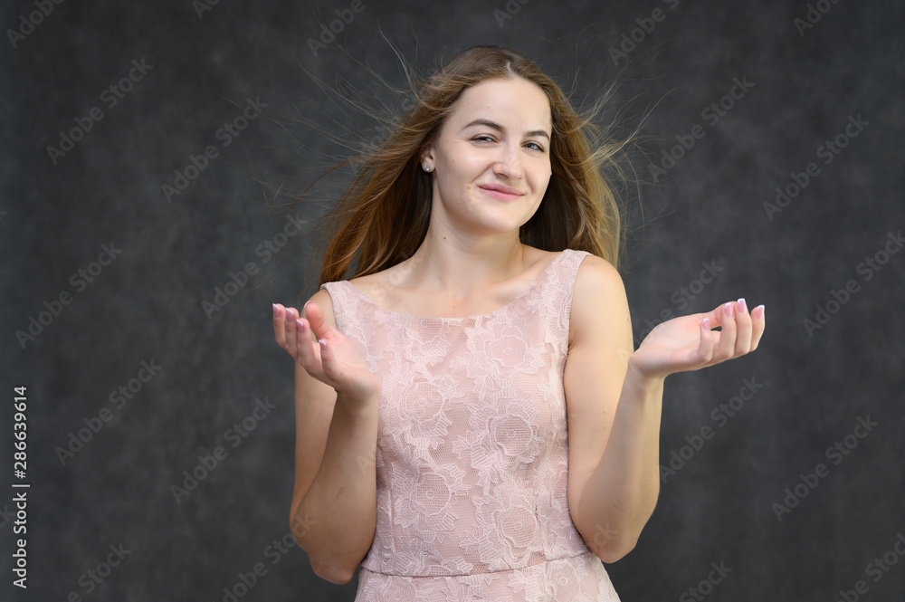 Studio portrait on the waist of a pretty student girl, a young brunette woman with long beautiful hair in a pink dress on a gray background. Smiling, talking, showing emotions Studio portrait on the waist of a pretty student girl, a young brunette woman with long beautiful hair in a pink dress on a gray background. Smiling, talking, showing emotions