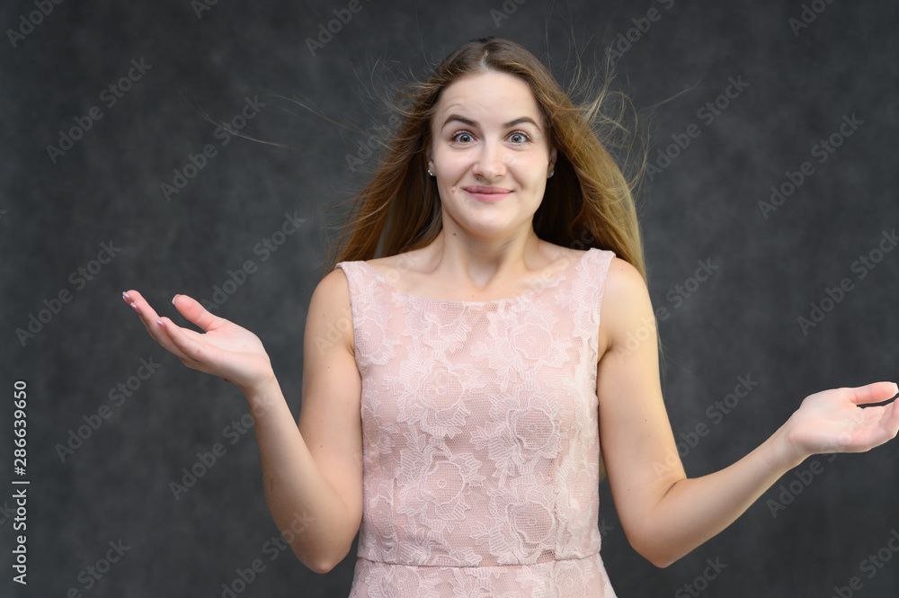 Studio portrait on the waist of a pretty student girl, a young brunette woman with long beautiful hair in a pink dress on a gray background. Smiling, talking, showing emotions Studio portrait on the waist of a pretty student girl, a young brunette woman with long beautiful hair in a pink dress on a gray background. Smiling, talking, showing emotions