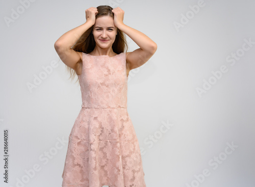 Studio portrait of a knee-length of a pretty girl student, brunette young woman with long beautiful hair in a pink dress on a white background. Smiling, talking, showing emotions photo