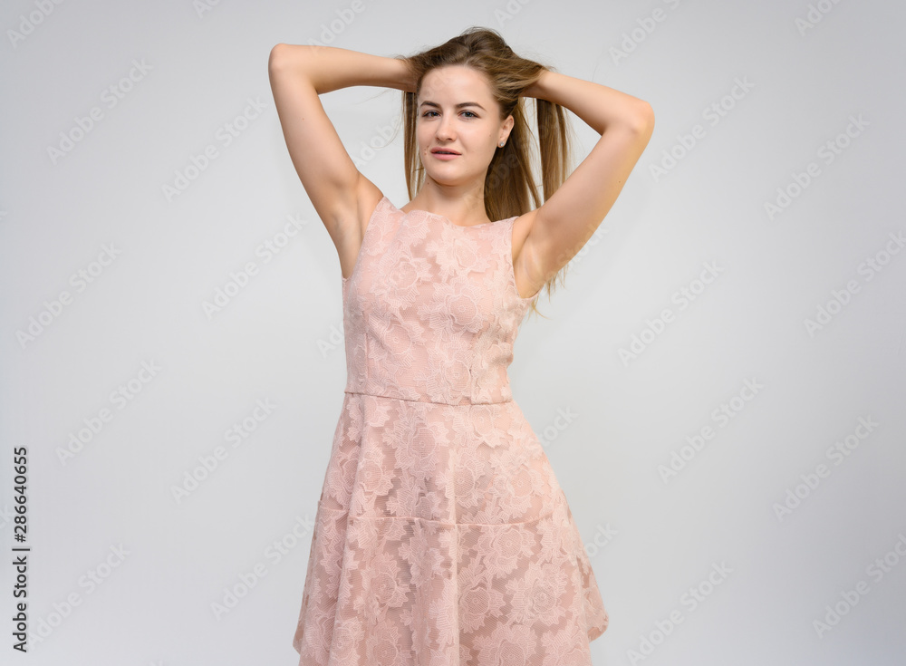Studio portrait of a knee-length of a pretty girl student, brunette young woman with long beautiful hair in a pink dress on a white background. Smiling, talking, showing emotions Studio portrait of a knee-length of a pretty girl student, brunette young woman with long beautiful hair in a pink dress on a white background. Smiling, talking, showing emotions