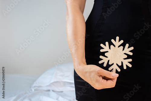 A woman holds a snowflake in her genital area, symbolizing her sexual coldness (frigidity) and unwillingness to have sexual relations with her partner. Sexual problems in marriage concept.