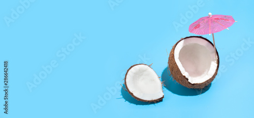 Fresh juicy coconut with a cocktail umbrella isolated on a blue background. Concept of Healthy eating and dieting. Travel and holiday concept. Copy space. Free space for your text