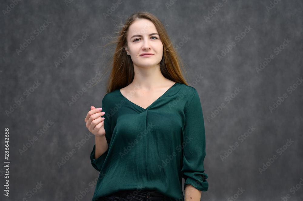 Studio portrait on the waist of a pretty student girl, a young brunette woman with long beautiful hair in a green blouse on a gray background. Smiling, talking, showing emotions Studio portrait on the waist of a pretty student girl, a young brunette woman with long beautiful hair in a green blouse on a gray background. Smiling, talking, showing emotions