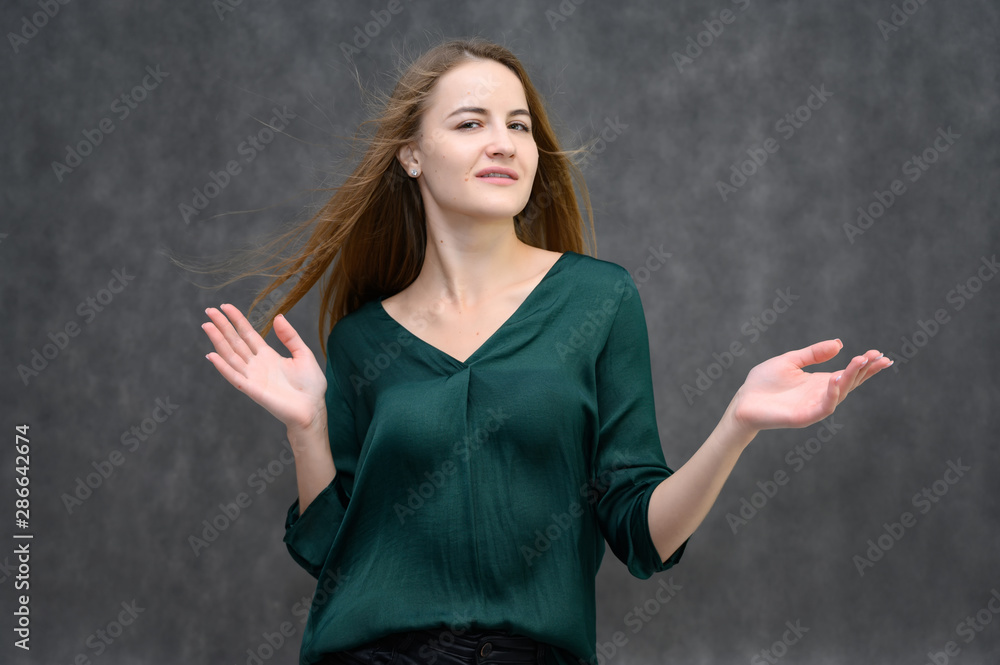 Studio portrait on the waist of a pretty student girl, a young brunette woman with long beautiful hair in a green blouse on a gray background. Smiling, talking, showing emotions Studio portrait on the waist of a pretty student girl, a young brunette woman with long beautiful hair in a green blouse on a gray background. Smiling, talking, showing emotions