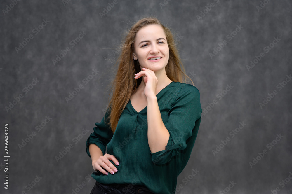 Studio portrait on the waist of a pretty student girl, a young brunette woman with long beautiful hair in a green blouse on a gray background. Smiling, talking, showing emotions Studio portrait on the waist of a pretty student girl, a young brunette woman with long beautiful hair in a green blouse on a gray background. Smiling, talking, showing emotions