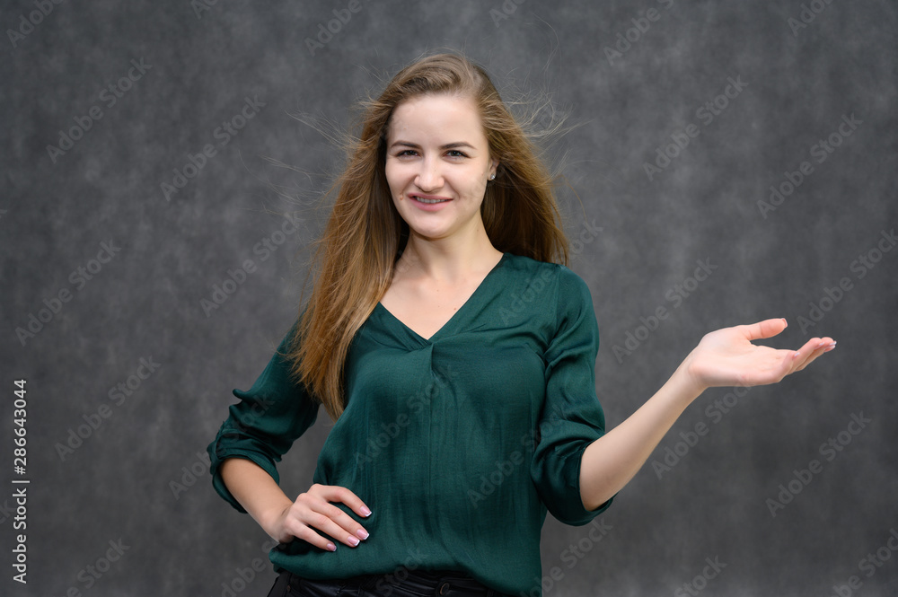 Studio portrait on the waist of a pretty student girl, a young brunette woman with long beautiful hair in a green blouse on a gray background. Smiling, talking, showing emotions Studio portrait on the waist of a pretty student girl, a young brunette woman with long beautiful hair in a green blouse on a gray background. Smiling, talking, showing emotions
