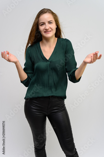 Studio portrait of a knee-length of a pretty student girl, a young brunette woman with long beautiful hair in a green blouse and black pants on a white background. Smiling, talking, showing emotions photo