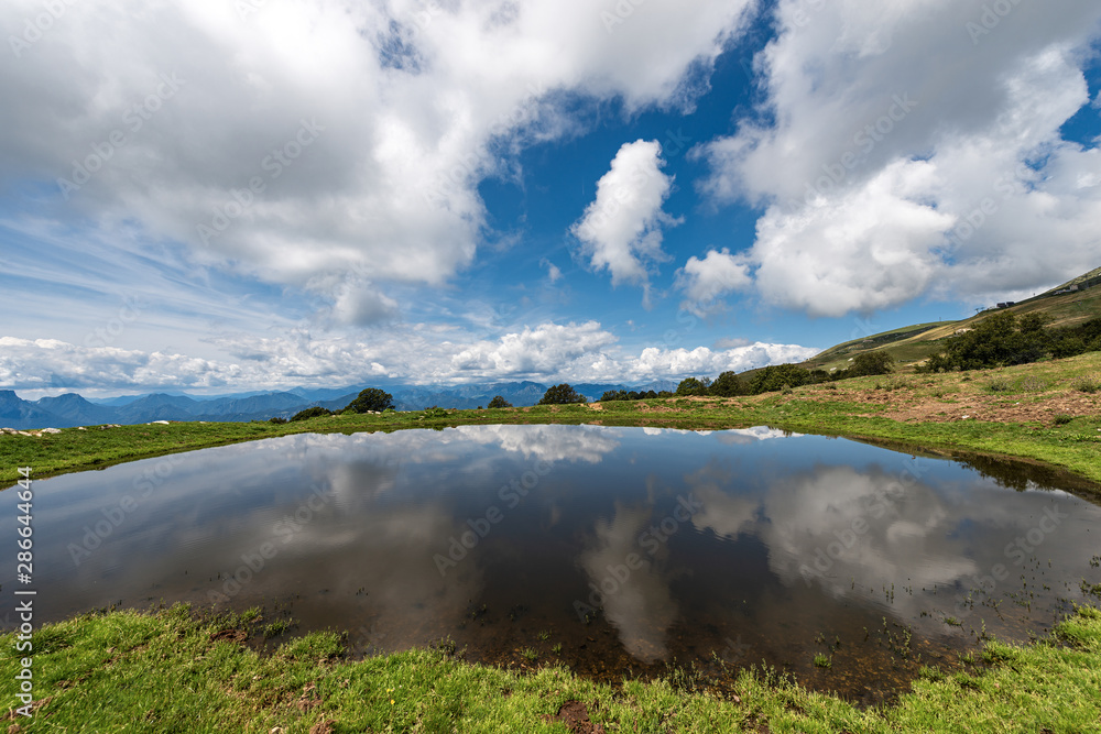 Small lake for livestock with reflections with sky and clouds, Monte Baldo, Italian Alps near Verona and lake Garda, Veneto, Italy, south Europe