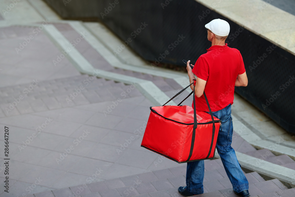 Man of takeaway with red insulated food bag in hand. Courier delivering food. Pizza delivery man carries breakfast, lunch, dinner for consumers. Express food delivery service from cafes, restaurants
