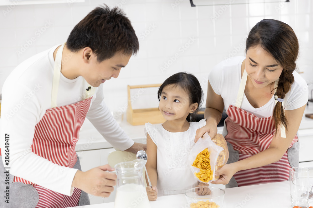 Happy Asian family make a cooking. Father and Mother make breakfast, cereal with milk give daughter in the kitchen at home. Healthy food concept For the strength of the body Happy Asian family make a cooking. Father and Mother make breakfast, cereal with milk give daughter in the kitchen at home. Healthy food concept For the strength of the body