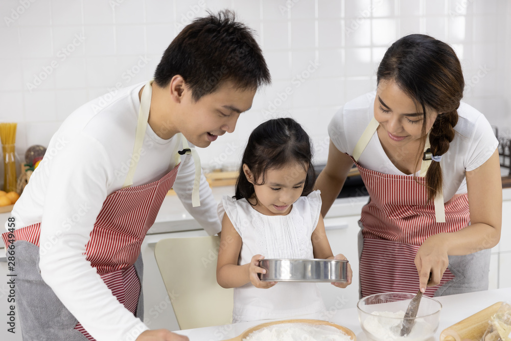 Happy Asian family Father, Mother and Daughter are sieving flour preparing the dough, bake cookies in the kitchen. family cooking food Concept. Happy Asian family Father, Mother and Daughter are sieving flour preparing the dough, bake cookies in the kitchen. family cooking food Concept.