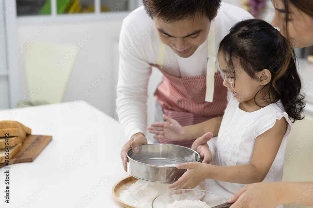 Happy Asian family Father, Mother and Daughter are sieving flour preparing the dough, bake cookies in the kitchen. family cooking food Concept. Happy Asian family Father, Mother and Daughter are sieving flour preparing the dough, bake cookies in the kitchen. family cooking food Concept.
