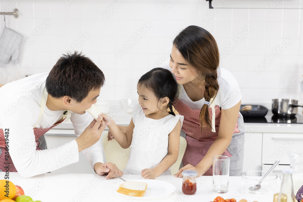 Happy Asian family make a cooking. Father, Mother and Daughter are eating breakfast in the kitchen at home. Bread with jam. Healthy food concept Happy Asian family make a cooking. Father, Mother and Daughter are eating breakfast in the kitchen at home. Bread with jam. Healthy food concept