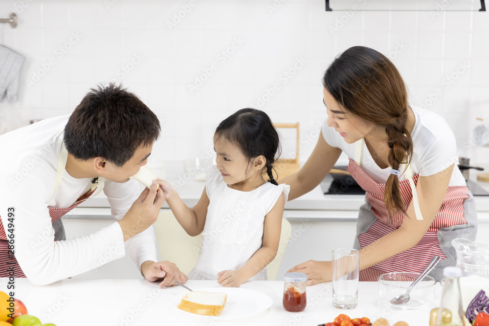 Happy Asian family make a cooking. Father, Mother and Daughter are eating breakfast in the kitchen at home. Bread with jam. Healthy food concept Happy Asian family make a cooking. Father, Mother and Daughter are eating breakfast in the kitchen at home. Bread with jam. Healthy food concept