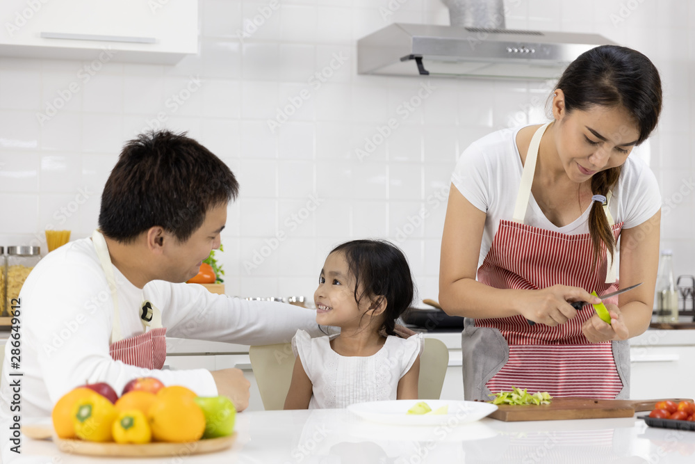Happy Asian family make a cooking. Father, Mother and Daughter are preparing fruit, green apple in the kitchen at home. Healthy food concept and happy holidays