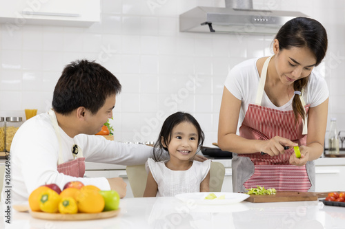 Happy Asian family make a cooking. Father  Mother and Daughter are preparing fruit  green apple in the kitchen at home. Healthy food concept and happy holidays