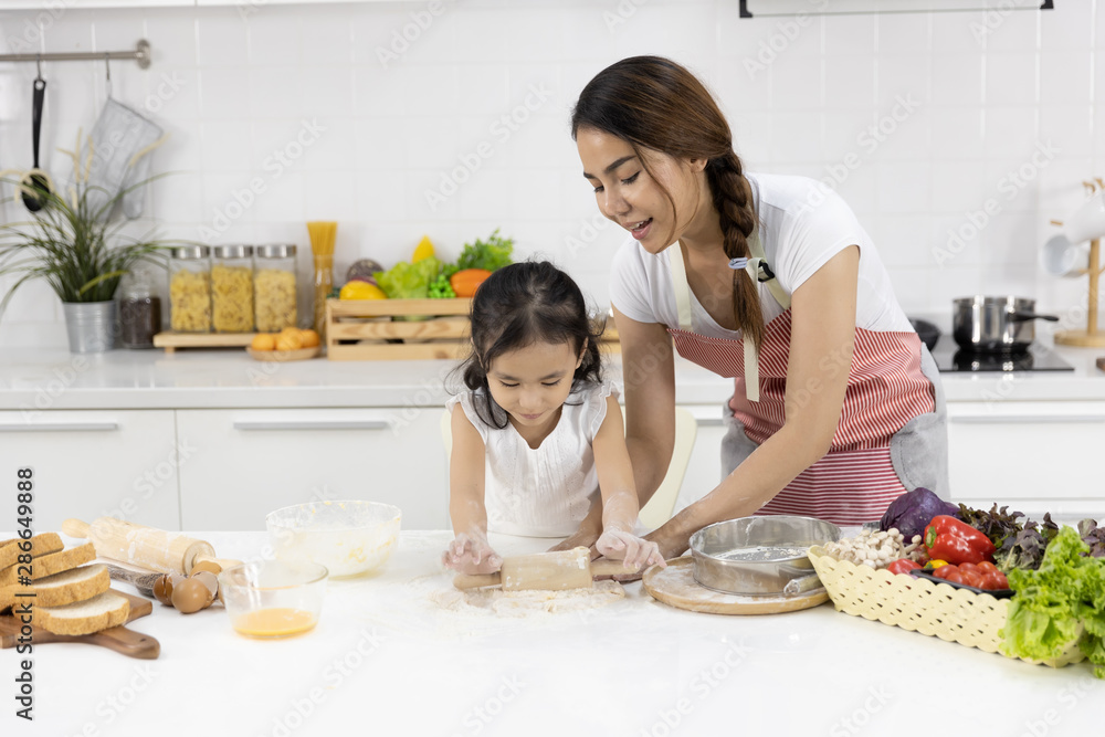 Happy Asian family Mother and Daughter are rolling pin thresh flour for making bakery in the kitchen in home. family cooking food Concept.