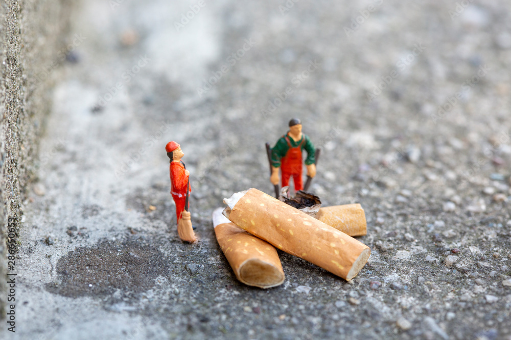 Obraz premium Two miniature garbage men cleaning and sweeping smoked cigarettes on the street which pollute the enviroment