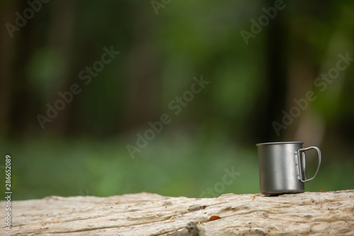 Travel titanium cup on wood on forest background.