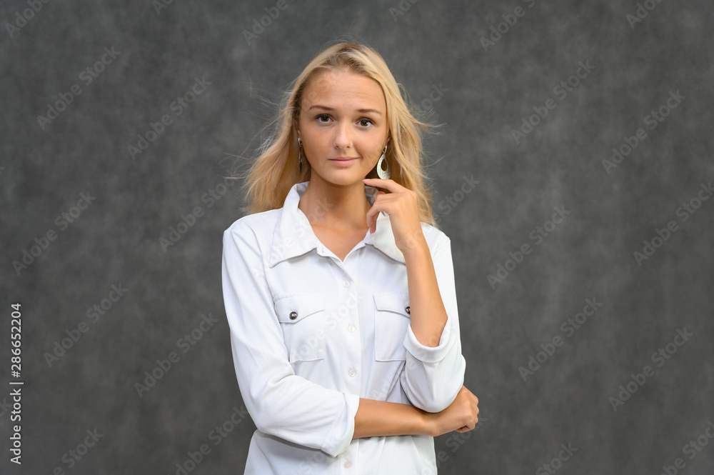 Studio portrait of a pretty blonde student girl, young woman in a white shirt on a gray background. Talking, showing emotions. Studio portrait of a pretty blonde student girl, young woman in a white shirt on a gray background. Talking, showing emotions.