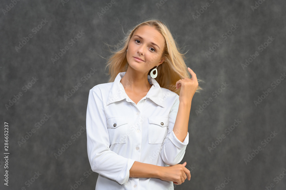 Studio portrait of a pretty blonde student girl, young woman in a white shirt on a gray background. Talking, showing emotions. Studio portrait of a pretty blonde student girl, young woman in a white shirt on a gray background. Talking, showing emotions.
