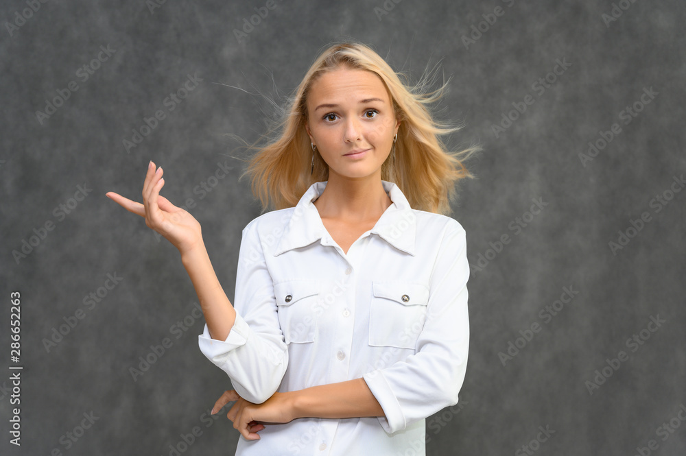 Studio portrait of a pretty blonde student girl, young woman in a white shirt on a gray background. Talking, showing emotions. Studio portrait of a pretty blonde student girl, young woman in a white shirt on a gray background. Talking, showing emotions.