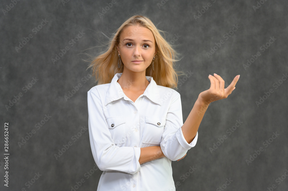 Studio portrait of a pretty blonde student girl, young woman in a white shirt on a gray background. Talking, showing emotions. Studio portrait of a pretty blonde student girl, young woman in a white shirt on a gray background. Talking, showing emotions.