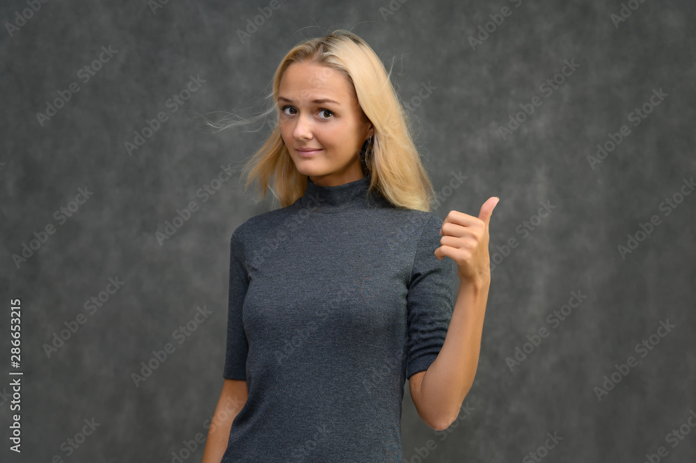 Studio portrait of a pretty blonde student girl, young woman in a gray sweater on a gray background. Talking, showing emotions. Studio portrait of a pretty blonde student girl, young woman in a gray sweater on a gray background. Talking, showing emotions.