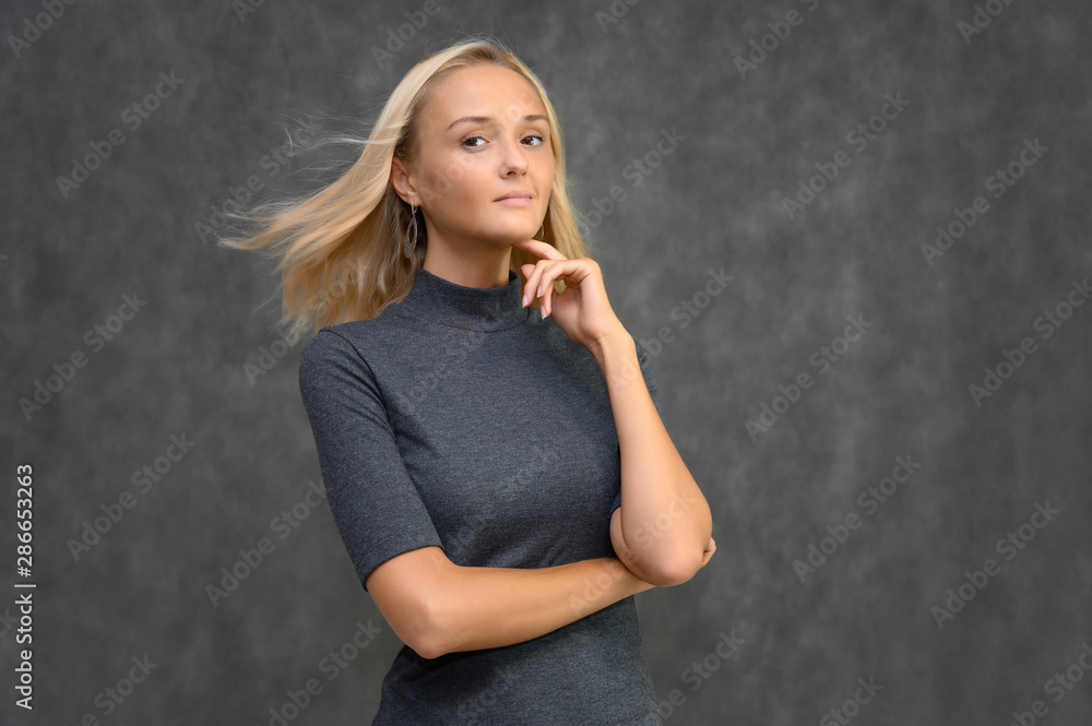 Obraz premium Studio portrait of a pretty blonde student girl, young woman in a gray sweater on a gray background. Talking, showing emotions.