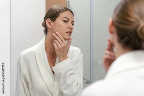 Woman in bathrobe looking in mirror at bathroom