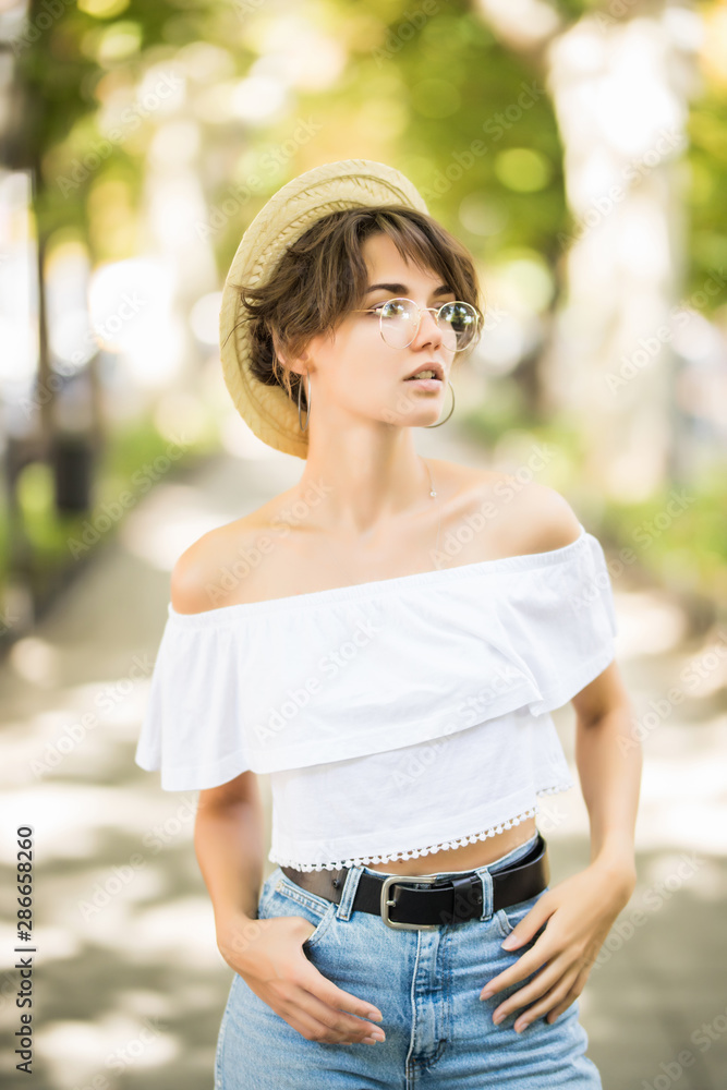 Young woman wearing straw hat while walking in green park Young woman wearing straw hat while walking in green park