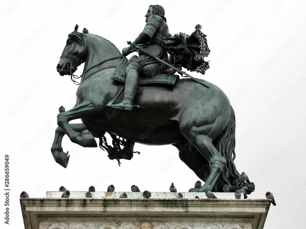 Equestrian statue in profile on white background. Pigeons sit on the statue. Spain, Madrid.