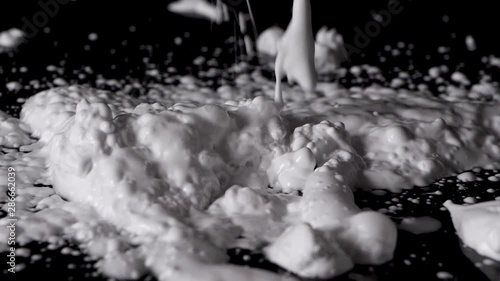 Shaving cream foam being poured from above onto a black bench and background in slow motion. photo