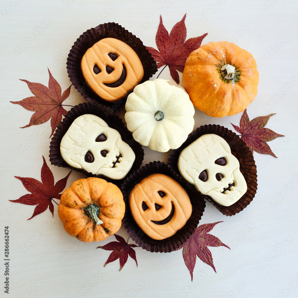 Funny Halloween jack-o-lantern and skull shaped shortbread sandwich cookies. mini pumpkins, dry autumn leaves.
