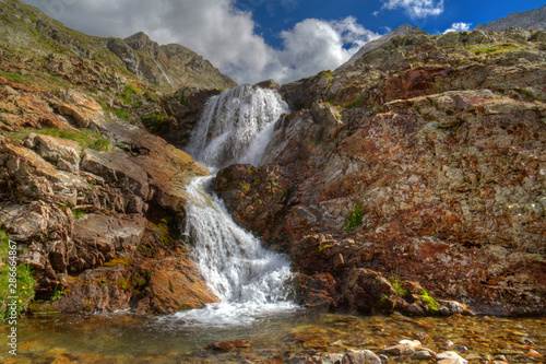 Small waterfall over red colored rocks and boulders  splashing in a small lake