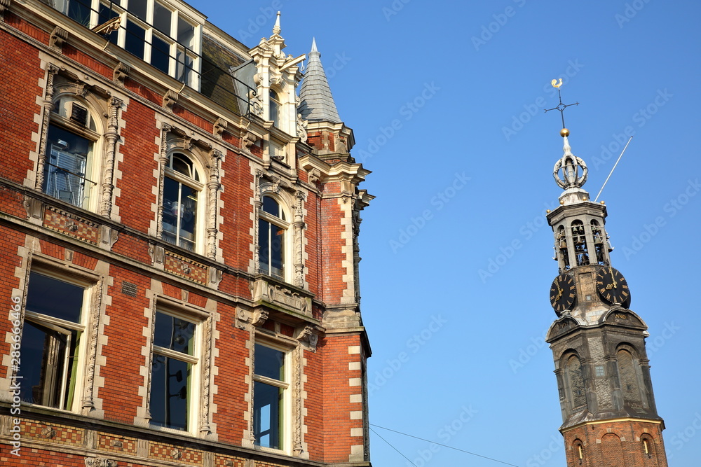 Close-up on Munttoren (historic tower with a carillon) and a colorful heritage building with carvings, Amsterdam, Netherlands