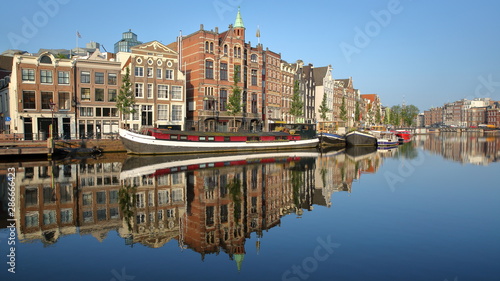 Crooked and colorful heritage buildings and houseboats, overlooking Amstel river with perfect reflections, Amsterdam, Netherlands