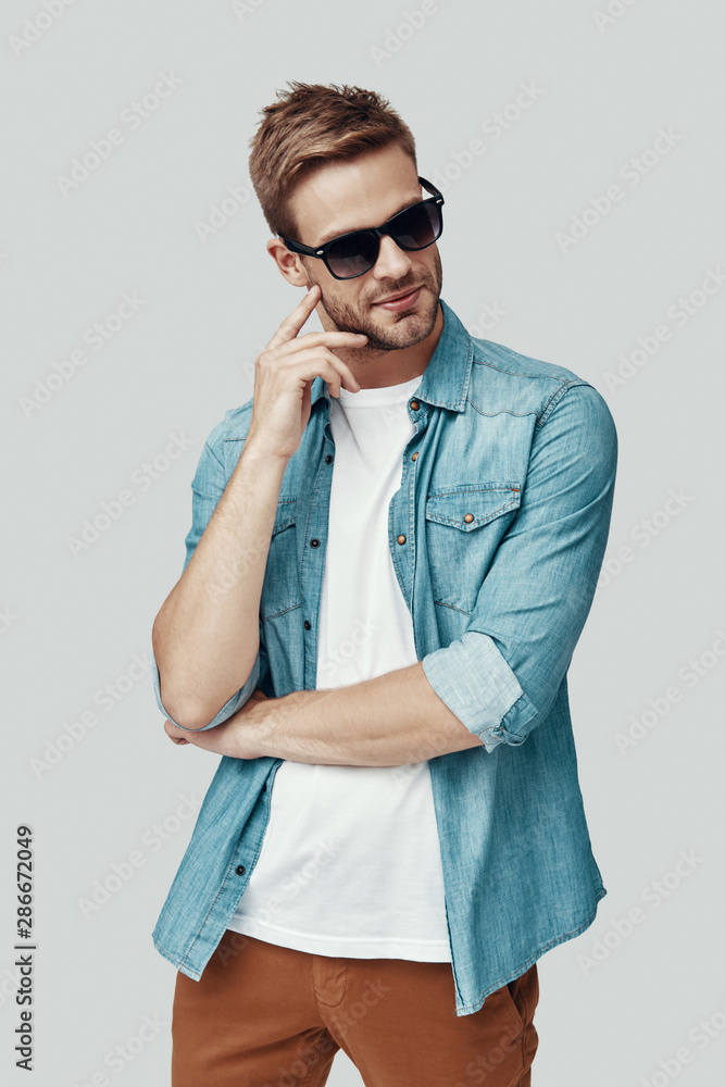 Handsome young man looking away and smiling while standing against grey background Handsome young man looking away and smiling while standing against grey background
