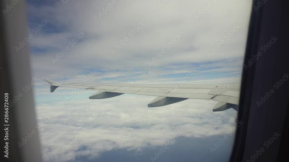 View from the porthole of an airplane on a blue sky and clouds. Airplane wing through the porthole. Looking through window aircraft during flight View from the porthole of an airplane on a blue sky and clouds. Airplane wing through the porthole. Looking through window aircraft during flight