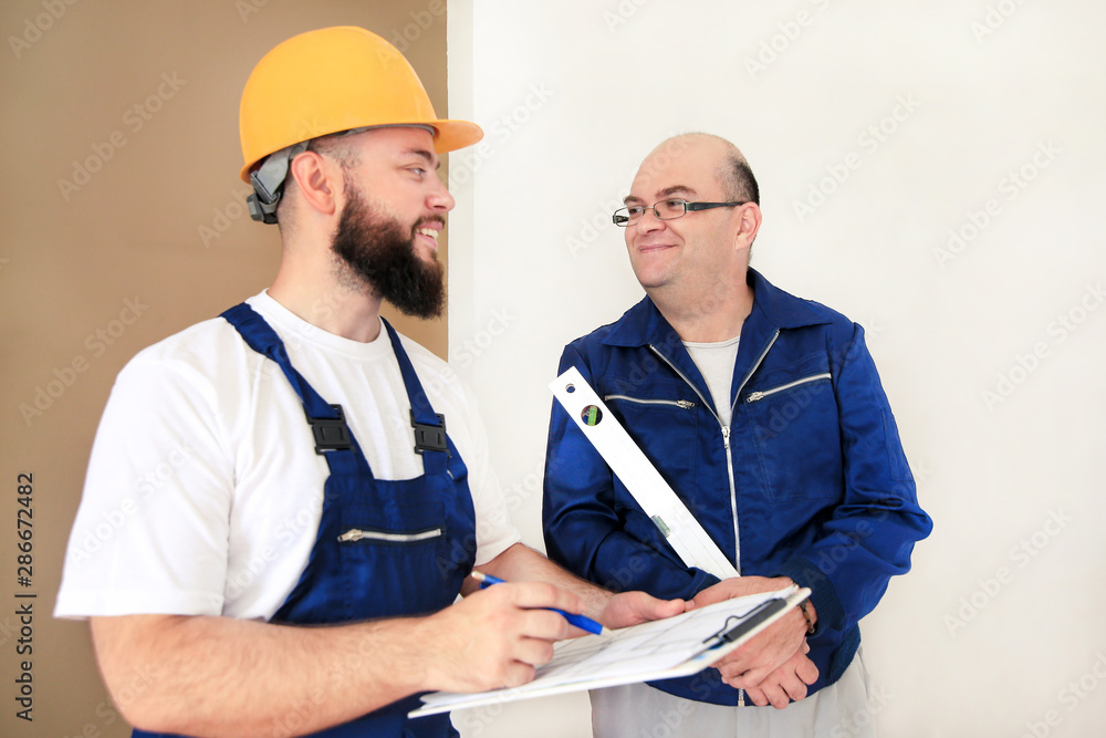Engineer, contractor and project manager with his colleague, construction worker, handyman and builder is measuring wall room for renovation using spirit level tool, checking in apartment blueprint. Engineer, contractor and project manager with his colleague, construction worker, handyman and builder is measuring wall room for renovation using spirit level tool, checking in apartment blueprint.