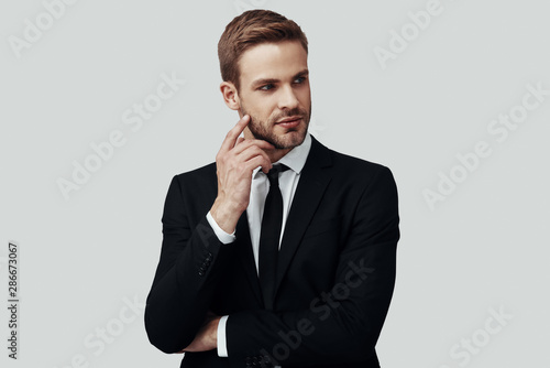 Handsome young man in formalwear looking away while standing against grey background