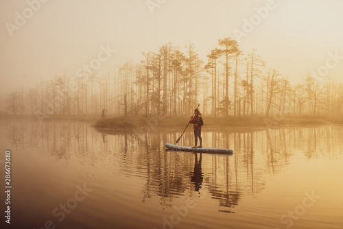 Woman slowly floating on the water on the sup-board. Fog and swamp.