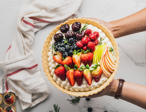 Hand holding Cake pie with strawberries blueberry on table food concept top view 