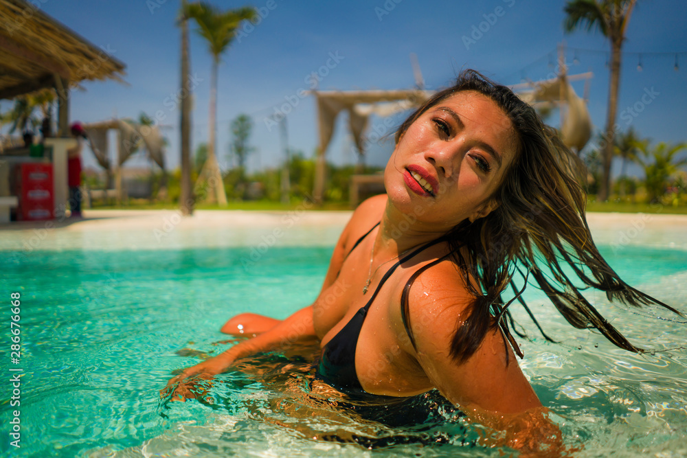 Naklejka premium young beautiful and happy Asian Indonesian woman in bikini swimming in tropical island pool resort enjoying luxury and exotic Summer holidays
