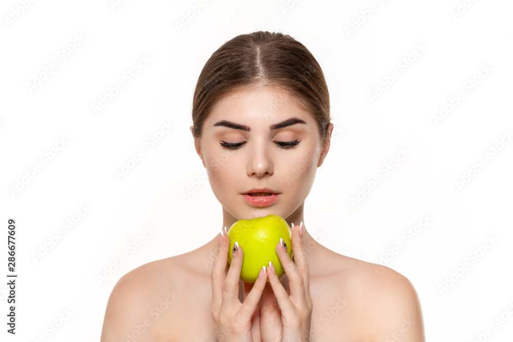 Close-up portrait of a happy beautiful young girl holding green apple close to face isolated over white background. Concept of beauty and health care. Close-up portrait of a happy beautiful young girl holding green apple close to face isolated over white background. Concept of beauty and health care.